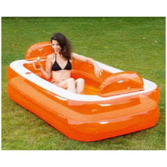 Woman in a black bikini relaxes in an orange inflatable pool with a white inner lining on green grass.