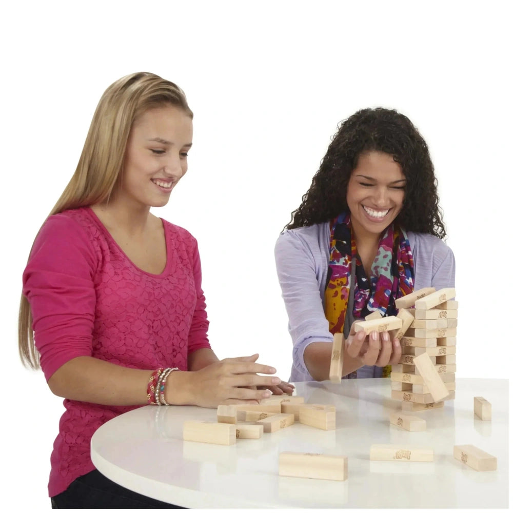 Jenga Family Game on a white table with two girls, one in a pink shirt, playing with wooden blocks.
