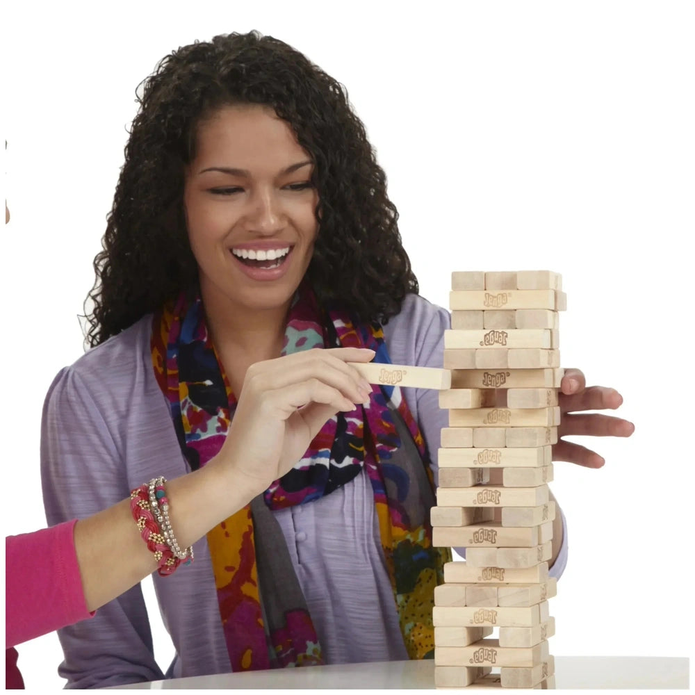 Woman in a purple top and colorful scarf smiles while holding a wooden Jenga block stacked on a white table.