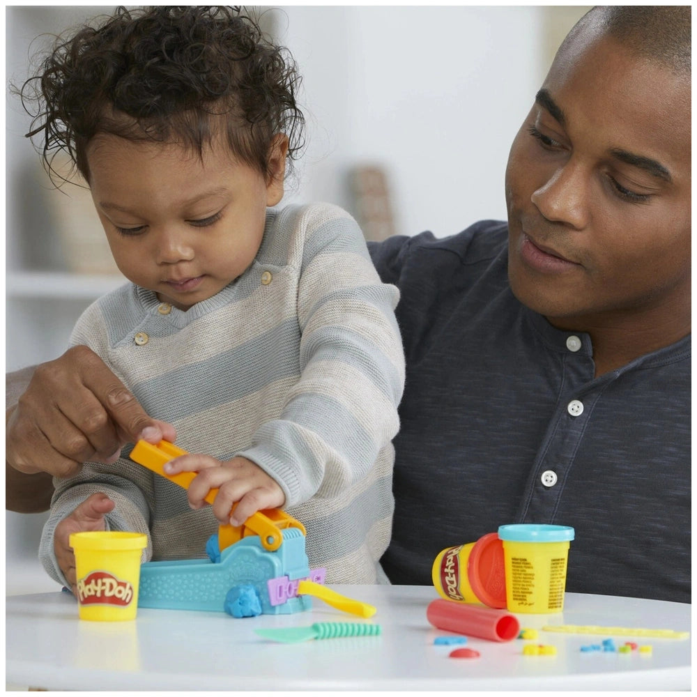 Play-Doh Fun Factory Starter Set displayed on a white tabletop with a man in a blue shirt and a child in a gray shirt.