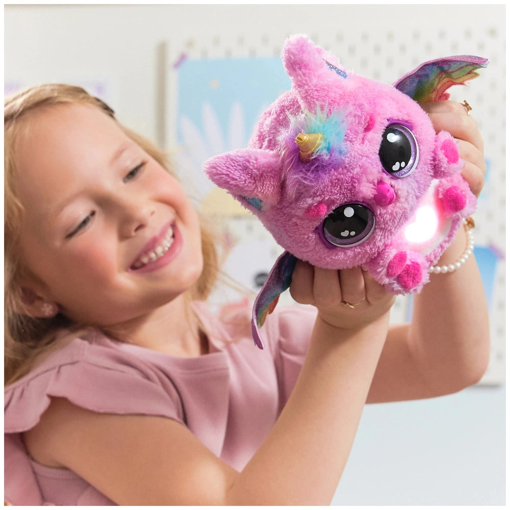 Hatchimals Alive Mystery Hatch Pufficorn plush toy in pink, purple, and blue held by a smiling girl indoors.