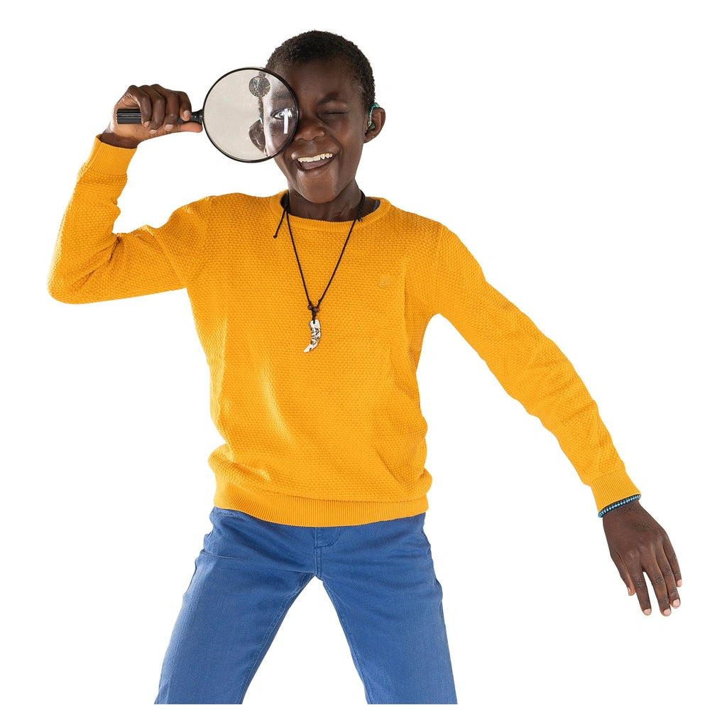 Johntoy Science Explorer magnifying glass held by a person in a yellow sweater and blue pants, with earbuds and a necklace.