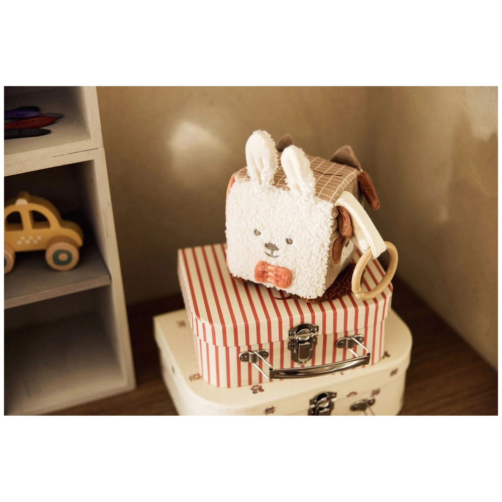 Jollein Activity Cube features a white plush stuffed animal with a bow tie, placed on a red and white striped suitcase.