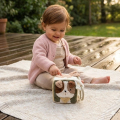 Jollein Activity Cube Tiny Park toy in front of a child sitting on a blanket on a wooden deck.