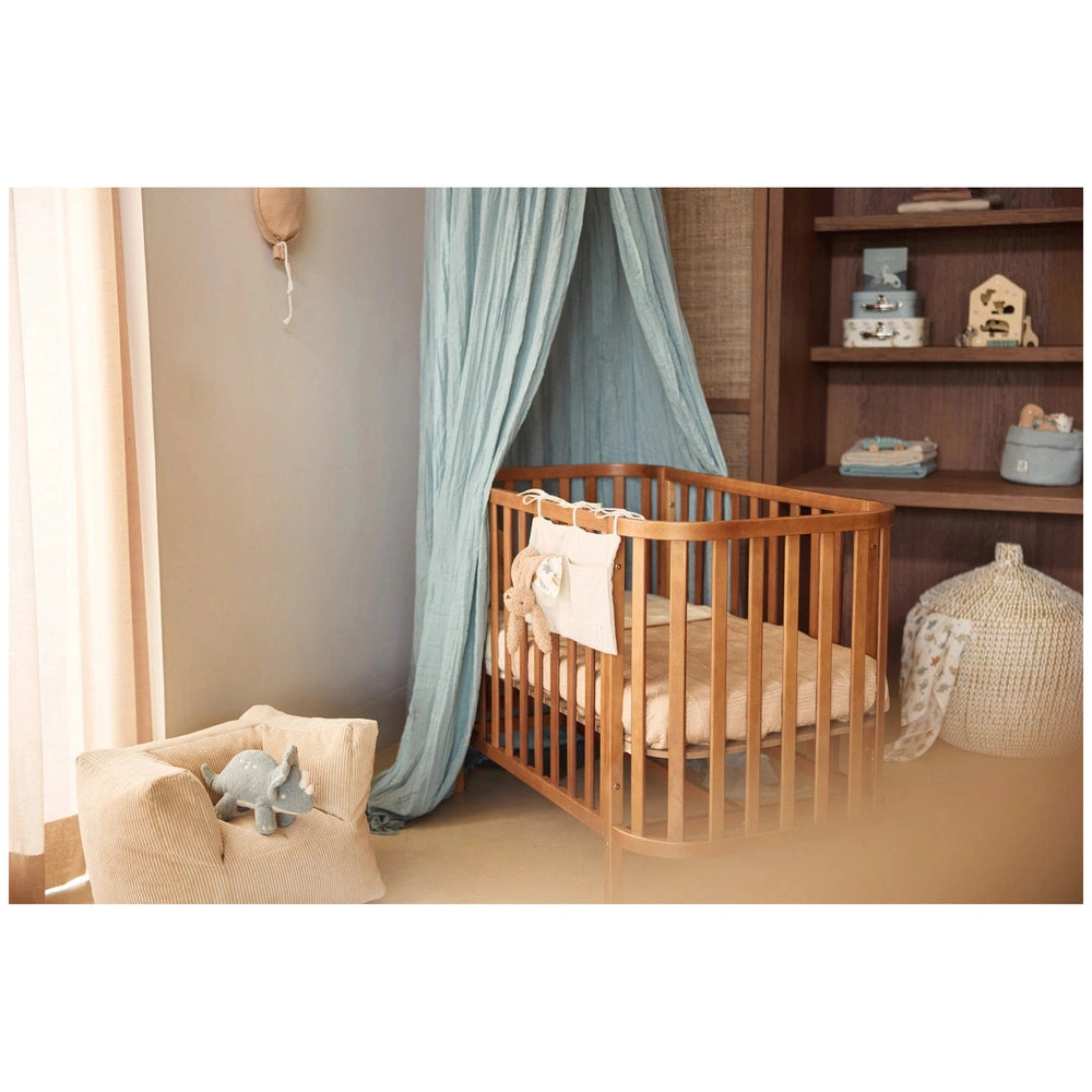 Jollein pacifier cloth bunny on a wooden crib with beige and light blue fabrics, creating a cozy nursery atmosphere.