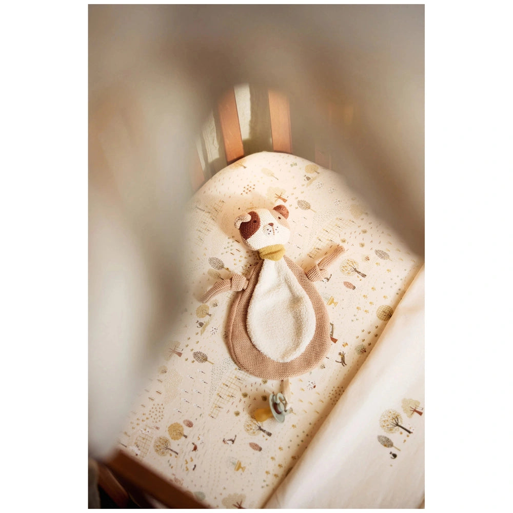 Jollein pacifier cloth Mick on a light-patterned bedsheet with a small brown bear wearing a white sweater and collar.