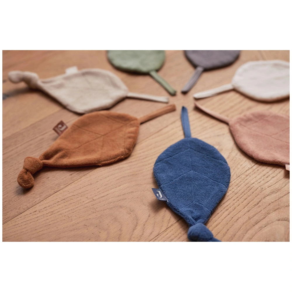 Jollein pacifier cloth features four colorful fabric paddles in brown, white, and blue, with blue cord strings attached.
