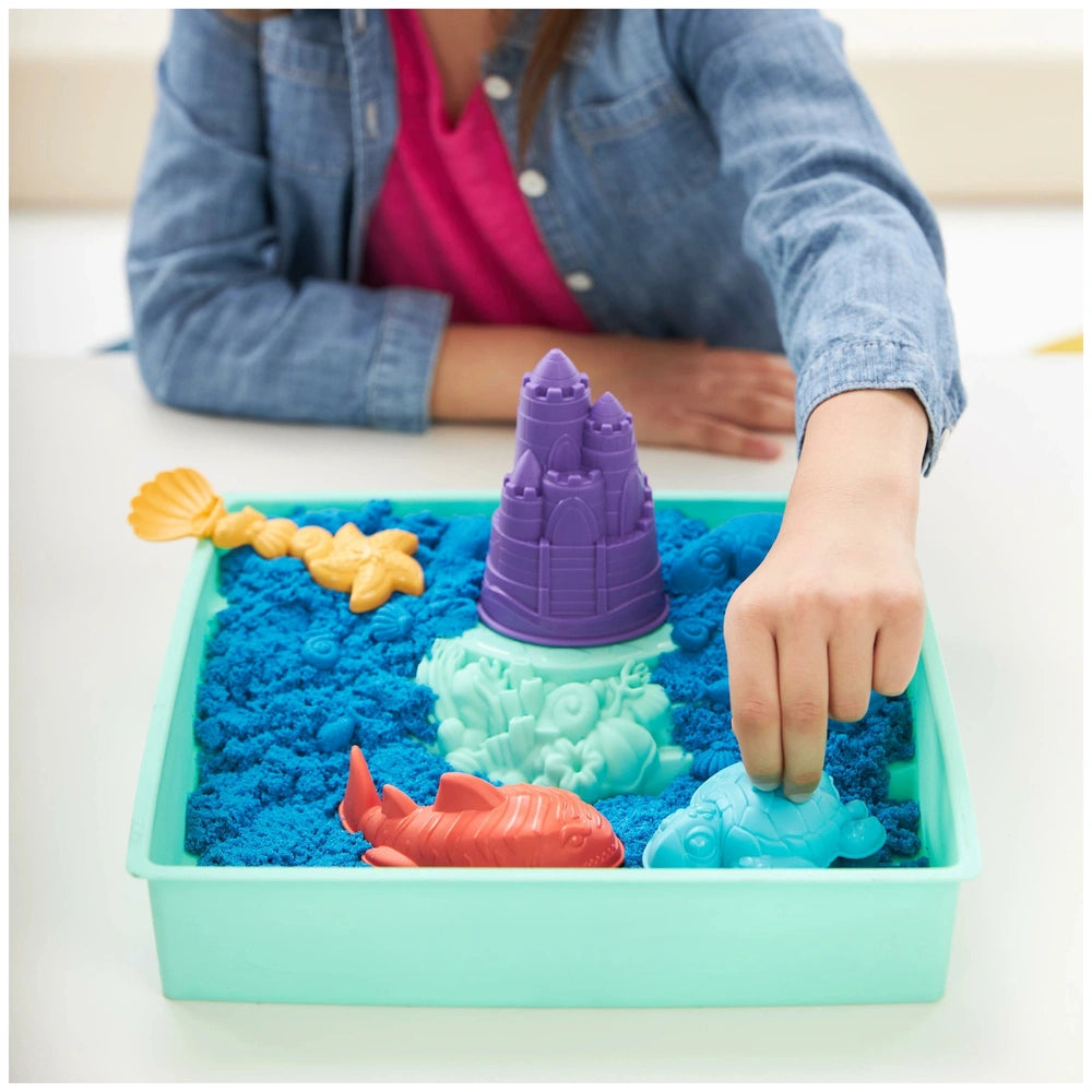 Kinetic Sand Sandbox Set features a purple castle toy surrounded by a yellow fish and red crab on a blue sandy surface.