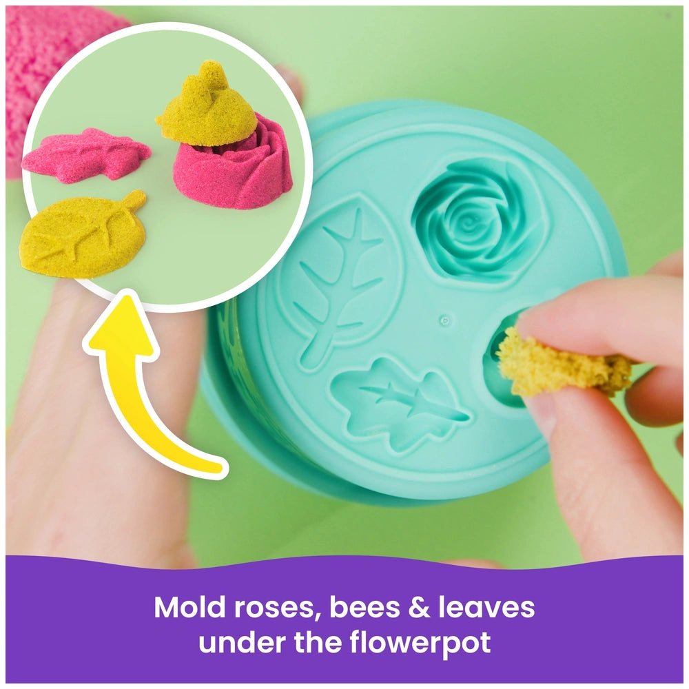 Kinetic Sand Squish Blossom features a green flowerpot container holding two pink rose-shaped objects on a green surface.