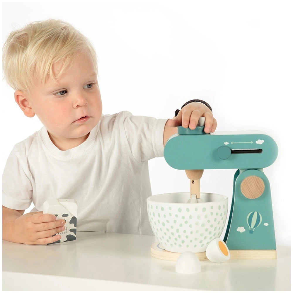 Child in a white t-shirt plays with a food processor toy on a white table, showcasing hands and fingers actively engaged.
