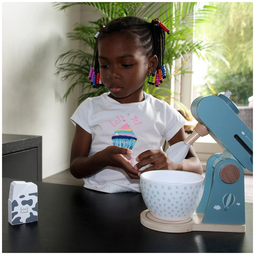 Young girl in braids wearing a graphic t-shirt holds a cupcake in front of a blue and white toy food processor.