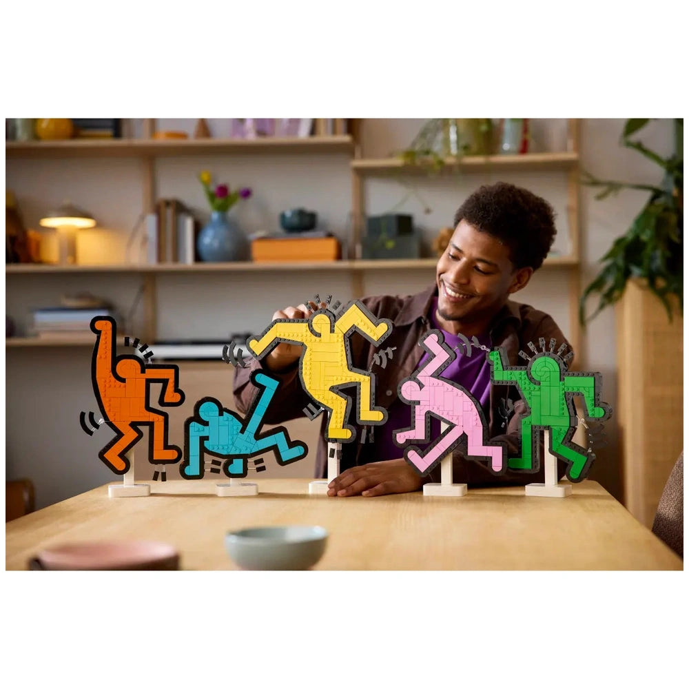 LEGO Art Keith Haring Dancing Figures displayed on a white stand, held by a smiling person in a brown jacket.