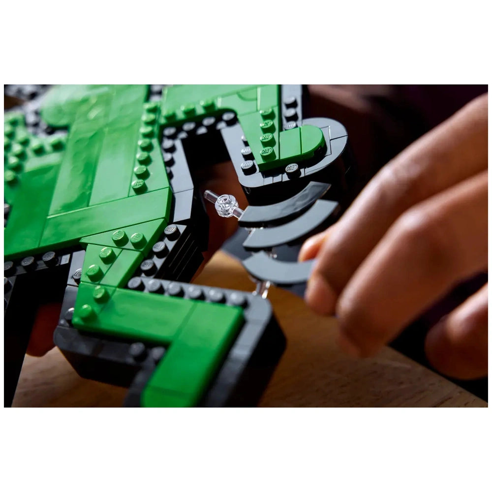 LEGO structure assembly features green and black pieces with glossy surfaces, showcasing a hand placing a piece.