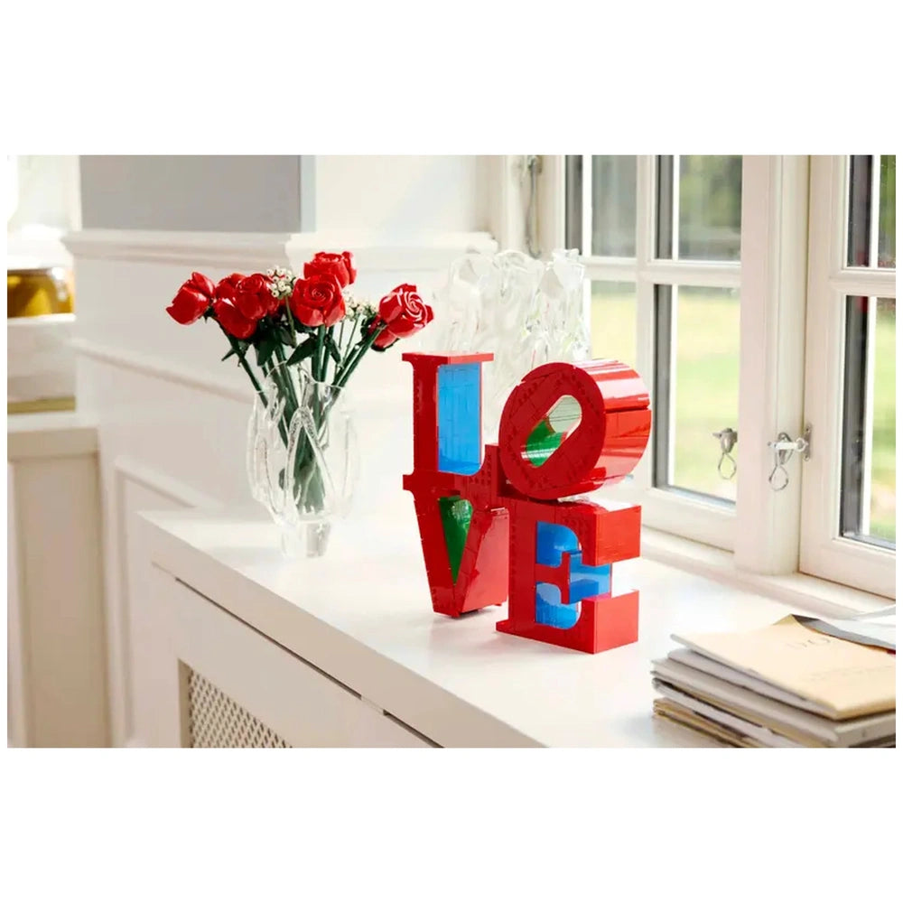 Lego Art LOVE construction set displayed on a white surface alongside a vase of red roses and a stack of papers.