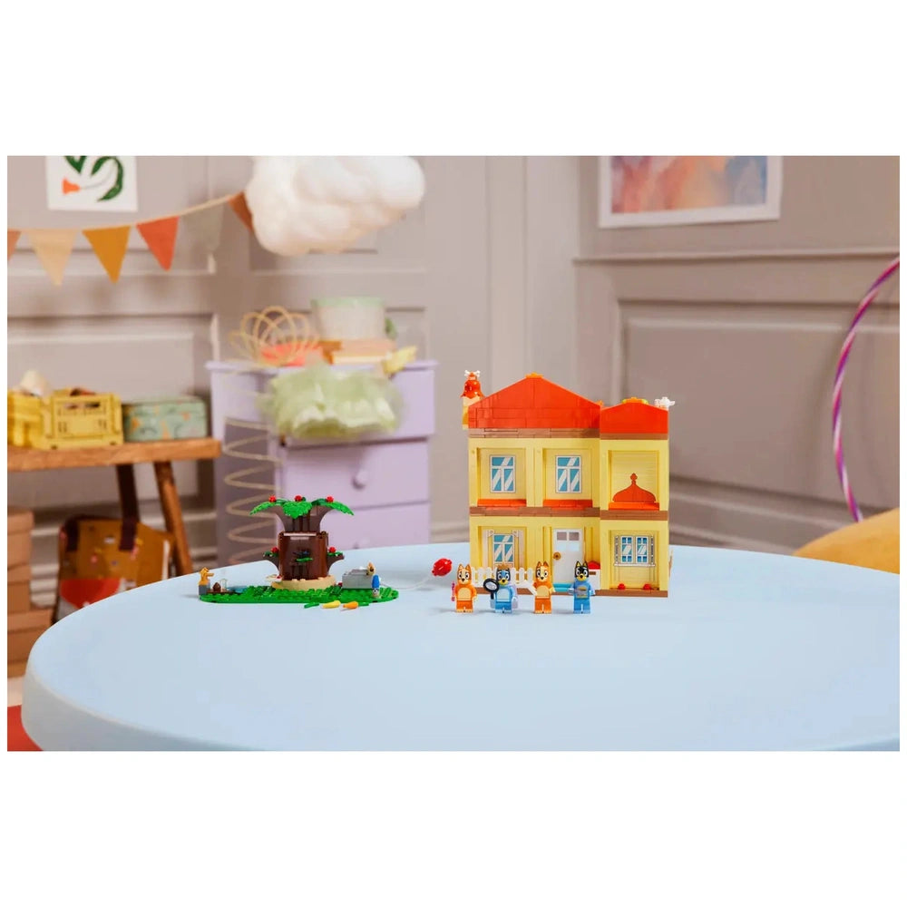 Colorful LEGO Bluey’s Family House playset on a light blue table, featuring four minifigures and a tree.