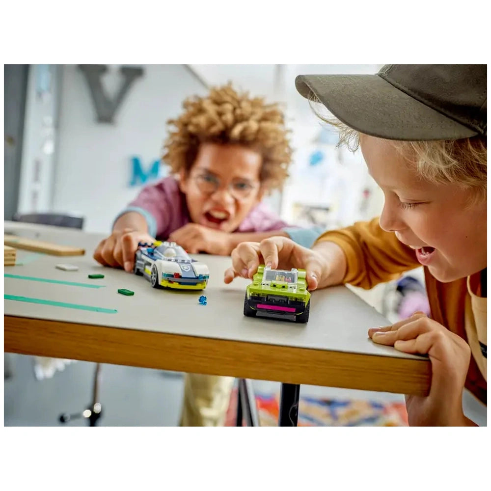 Two children excitedly play with LEGO® cars on a table, focusing on a police car and a muscle car, surrounded by building accessories.