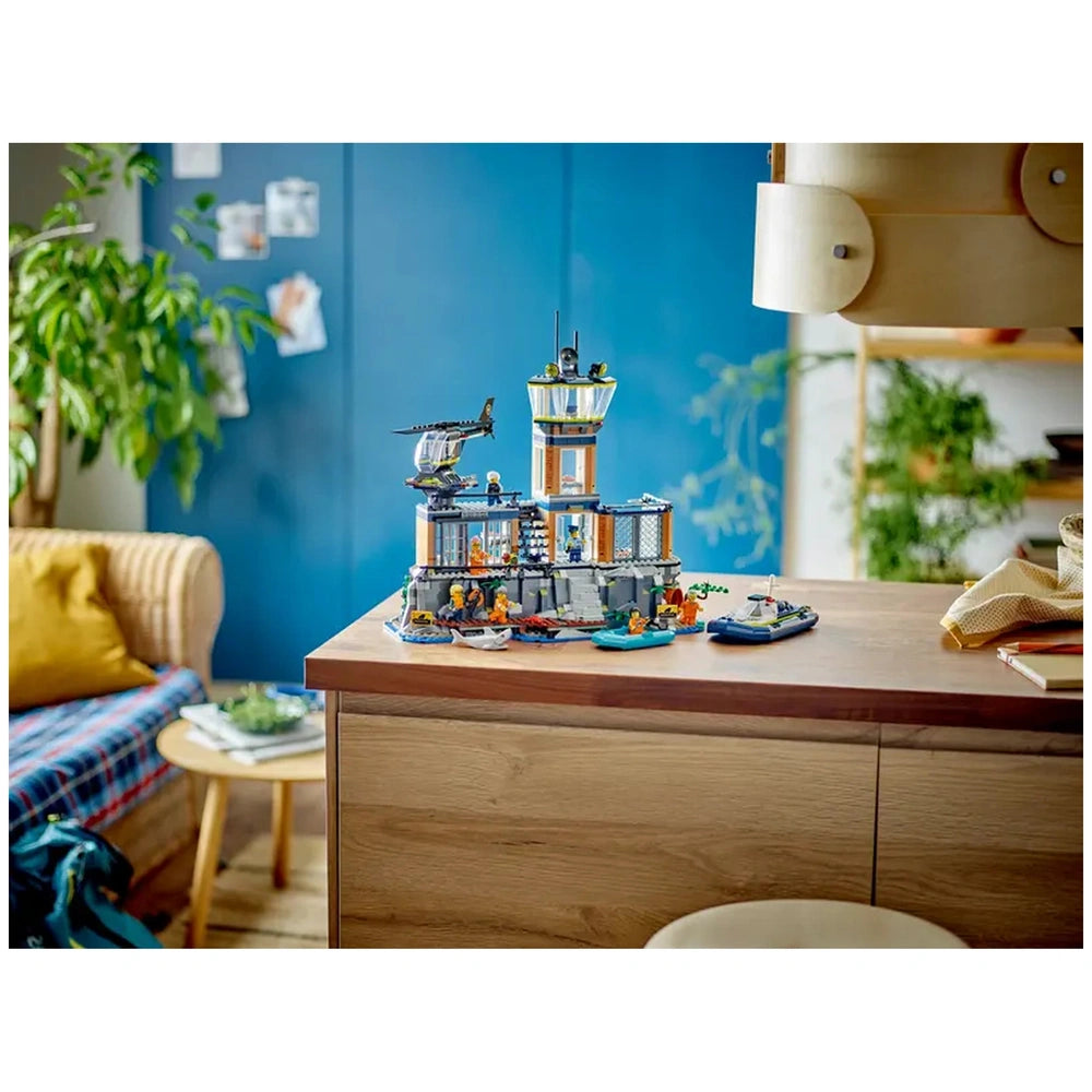 LEGO® City Police Prison Island set on a wooden table, featuring a detailed cliffside prison, officers, and escape boats, surrounded by foliage and cozy furniture.