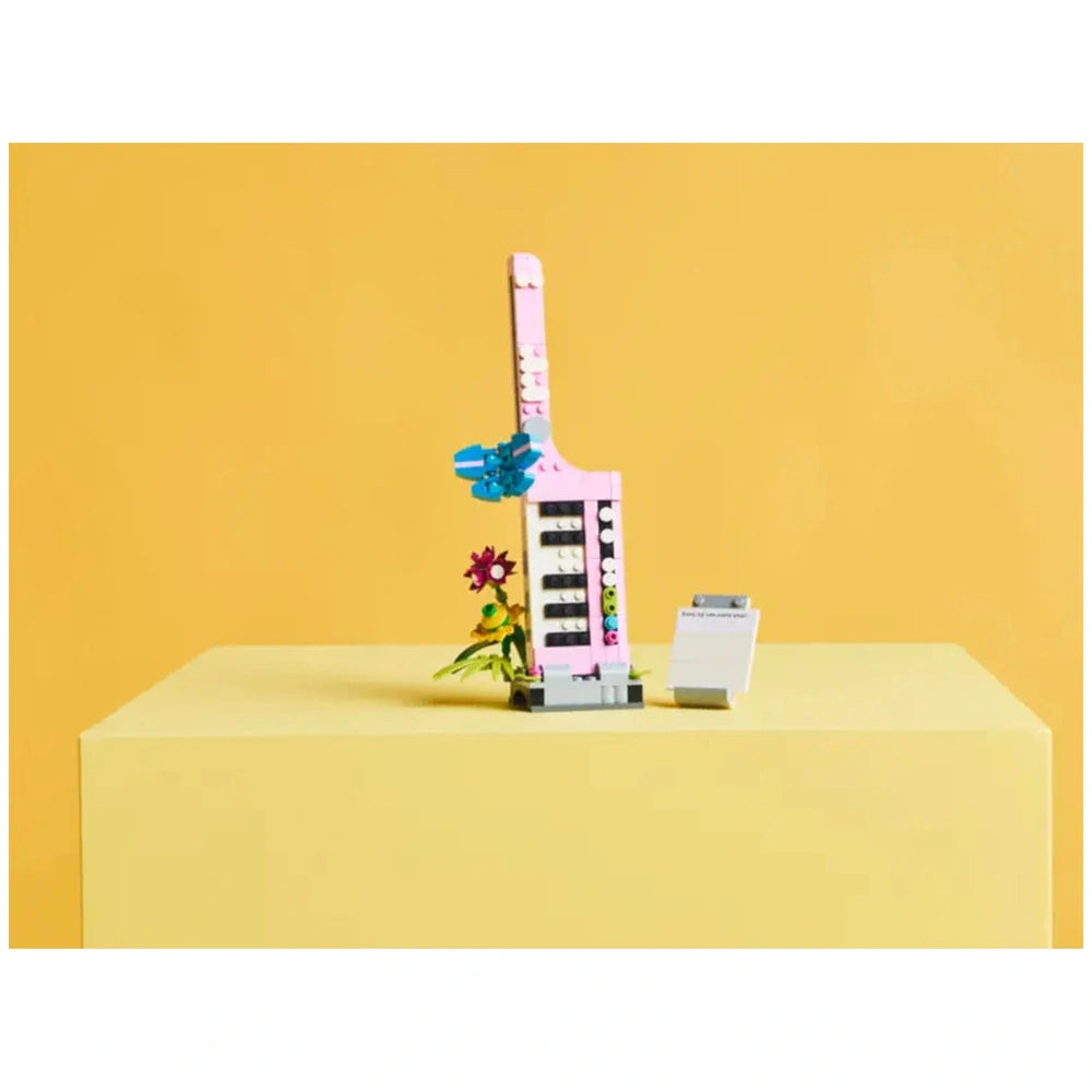 LEGO Creator 3in1 Typewriter with Flowers set, featuring a pink typewriter with colorful brick flowers and a small paper pad on a yellow background.