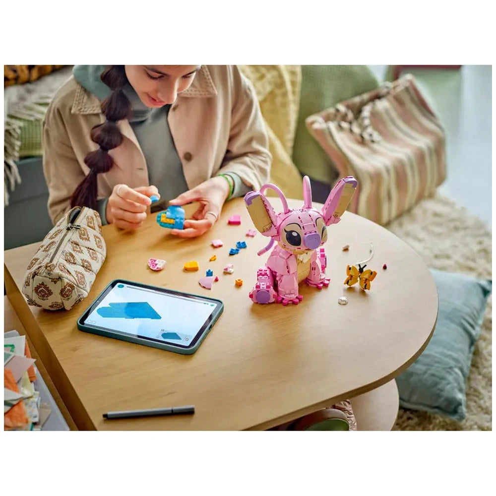 Creative child builds LEGO Disney Angel model on a wooden table, surrounded by colorful bricks and a tablet showing instructions. A butterfly and additional pieces are nearby.