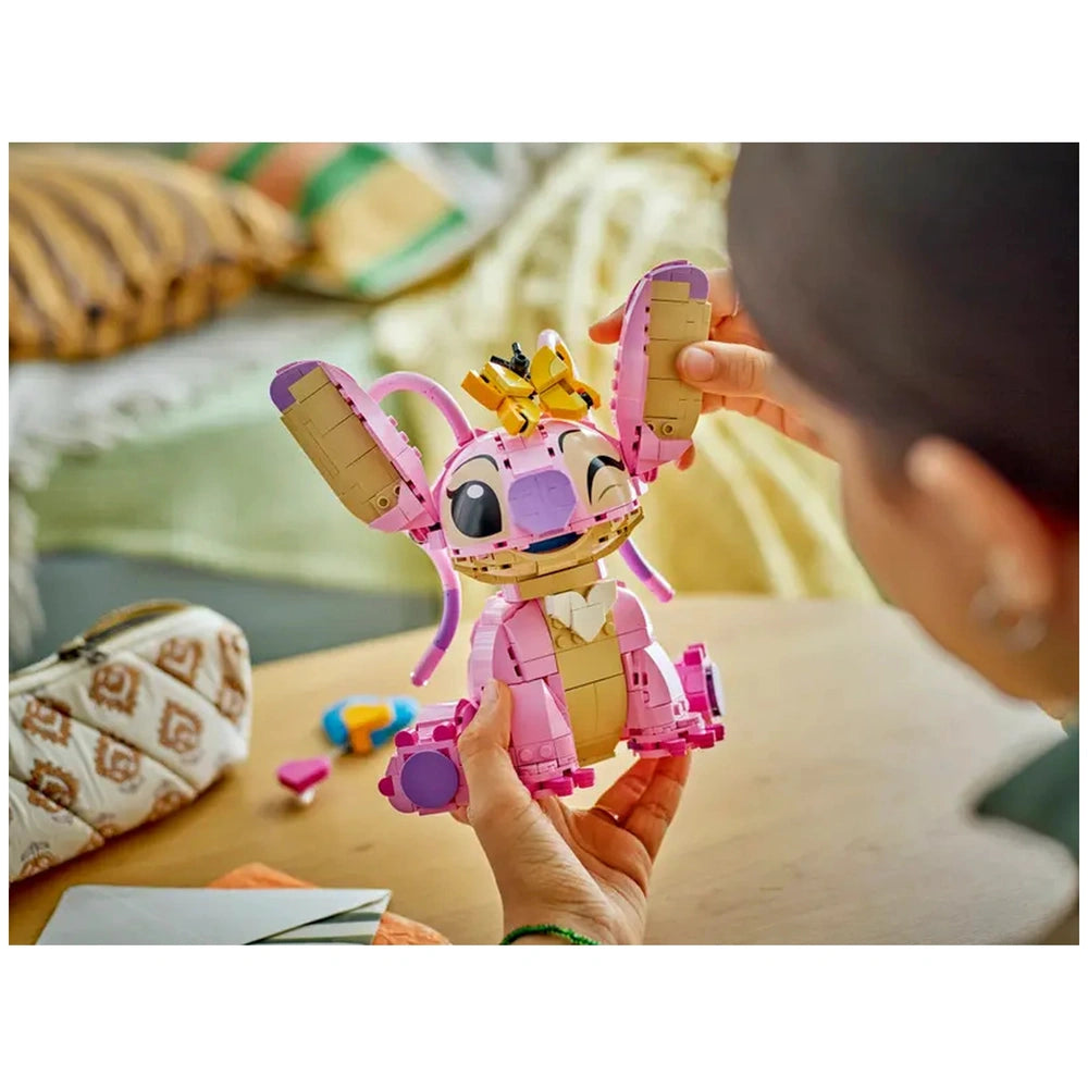 LEGO Angel character from Disney, featuring bright pink and beige colors, with movable ears and a playful expression, held by a child, surrounded by colorful toy pieces on a wooden table.