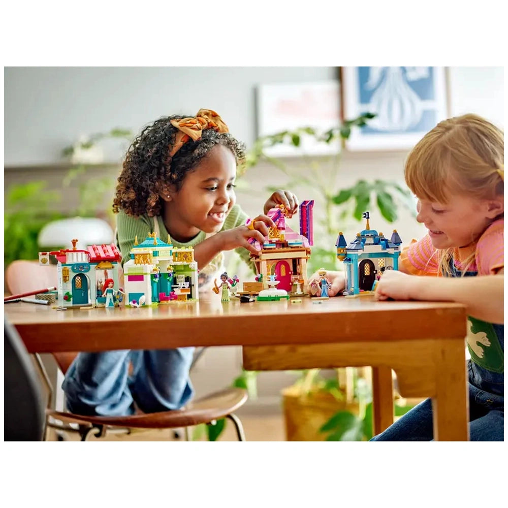 Two children joyfully playing with the LEGO Disney Princess Market Adventure set, featuring colorful toy buildings and miniature figures on a wooden table.