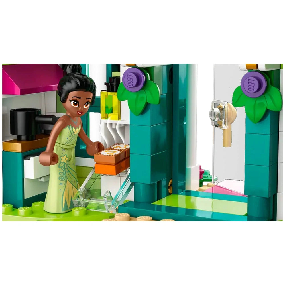 A Lego figure of Tiana in a green dress, smiling as she reaches for a box in a colorful kitchen setting from the Disney Princess Market Adventure set.