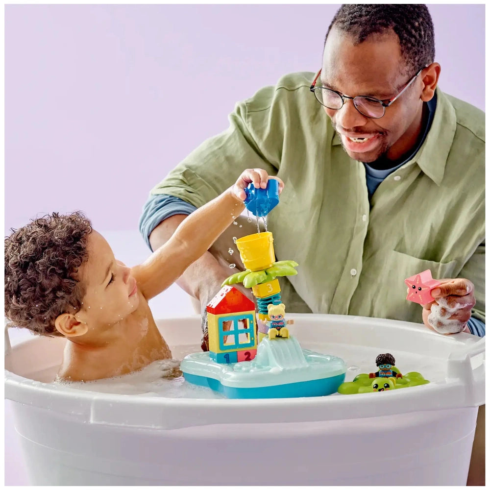 A toddler splashes water while stacking colorful building blocks at a vibrant toy water park, assisted by an adult.