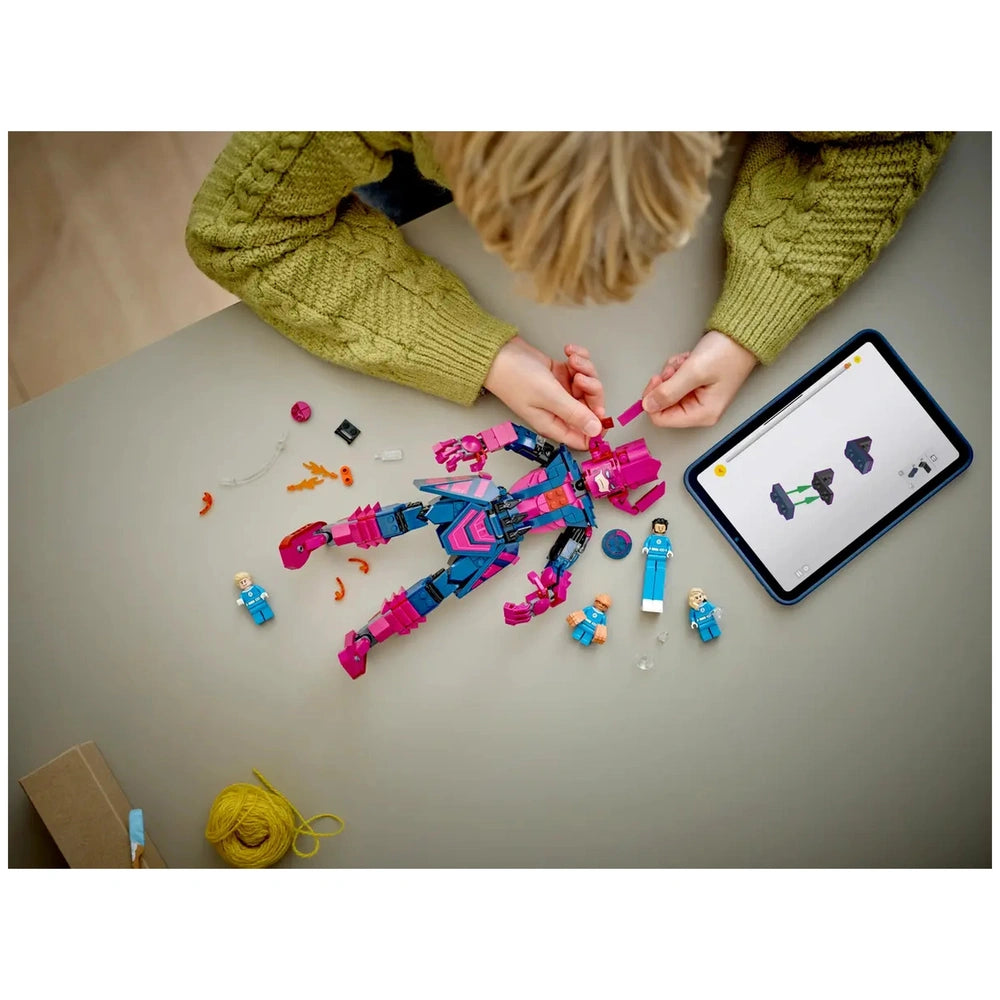 Child assembling a pink and blue LEGO figure with tiny parts scattered around, while following instructions on a tablet.