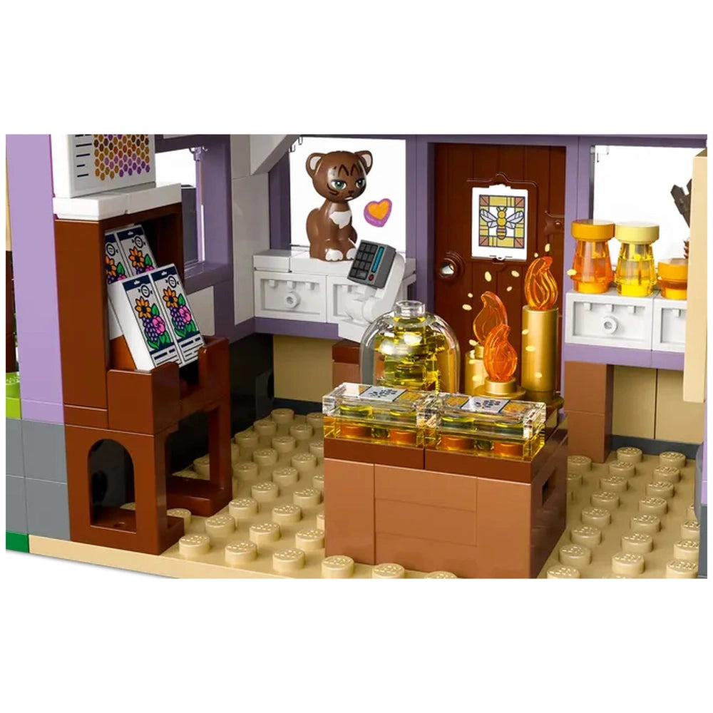 Interior view of the LEGO Friends Beekeepers' House, showcasing a cozy room with a brown bear figure, colorful flower-patterned books, honey jars, and decorative elements like flames. The warm tones and playful details create a charming atmosphere for imaginative play.