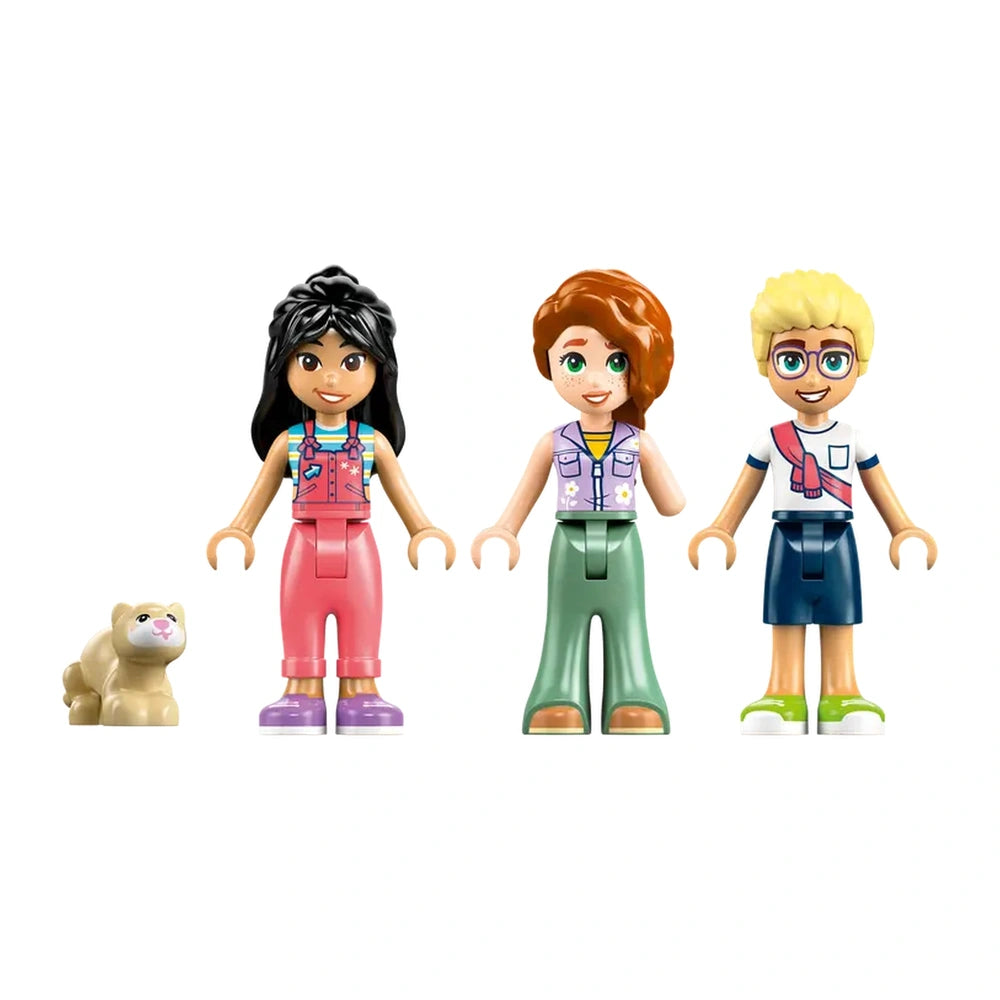 Three LEGO Friends minidolls stand side by side: a girl with black hair in pink overalls, a redhead in a green outfit, and a boy with blonde hair in a blue shirt. A small ferret figure sits nearby.