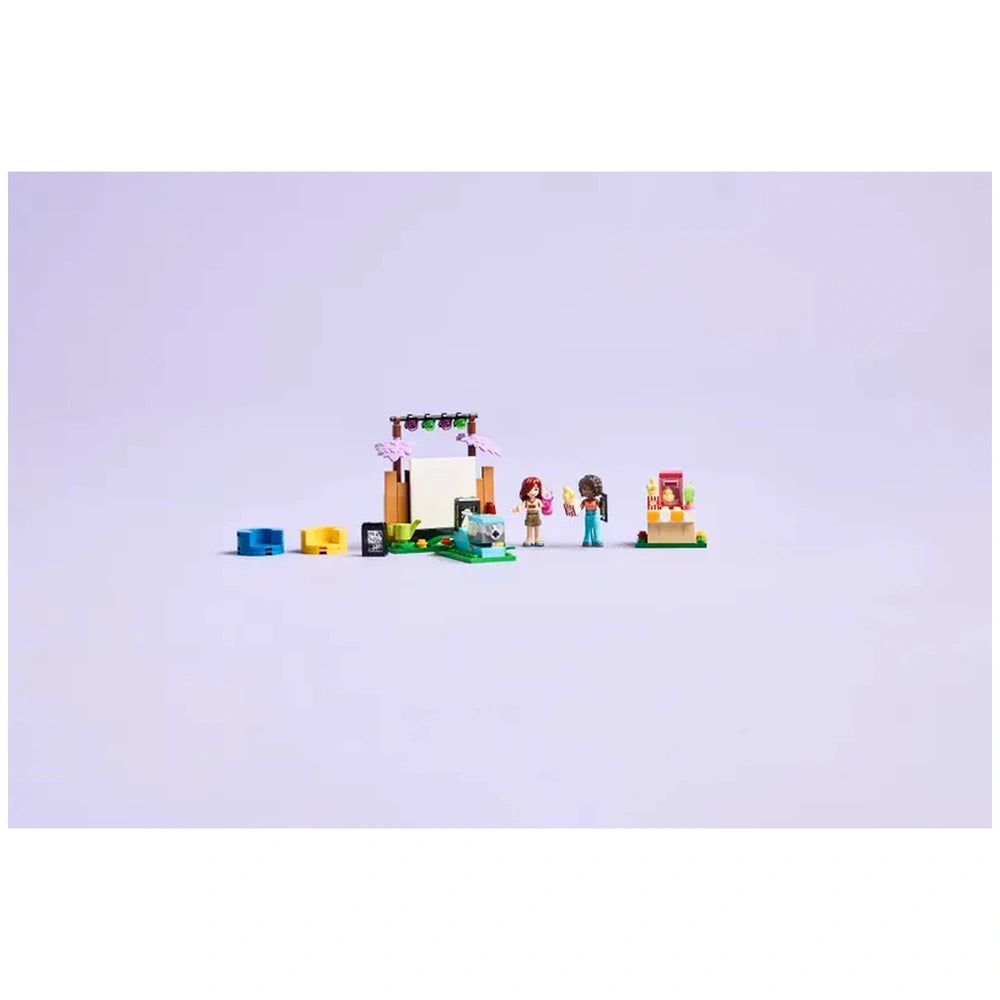 Two LEGO Friends minidolls, Paisley and Aliya, stand beside a mini projector in a garden setting, with colorful accessories for a movie night.