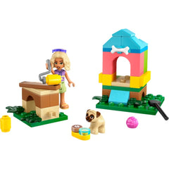 A cheerful minifigure with blonde hair stands next to a colorful doghouse construction set. A small pug features by a bowl and toys, surrounded by green baseplates and building elements.