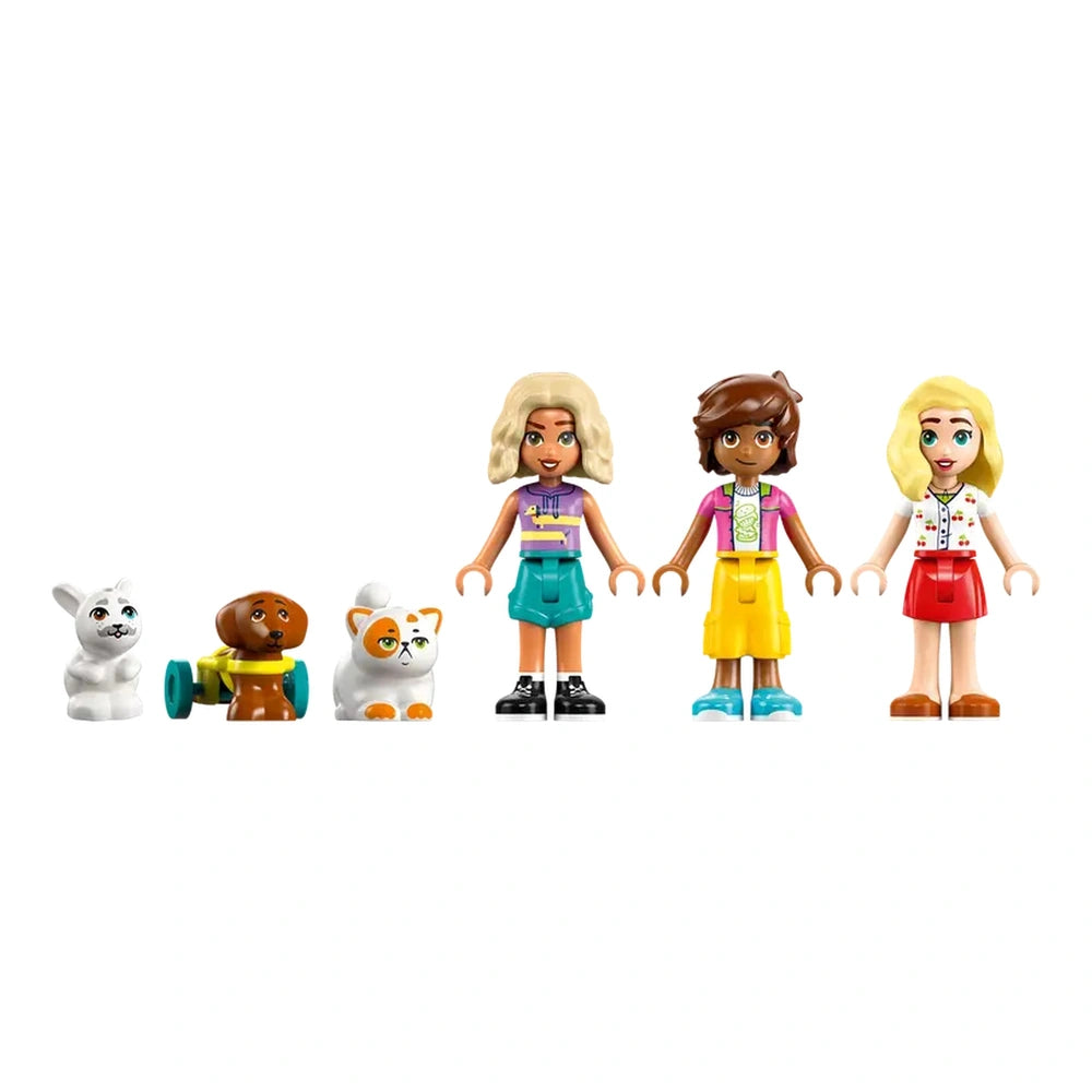 Three LEGO® Friends minidolls stand side by side, each dressed in colorful outfits. To their left, a white rabbit, a brown dog with a toy, and a cat with orange patches complete the scene. The background is plain, emphasizing the playful pet accessories theme.