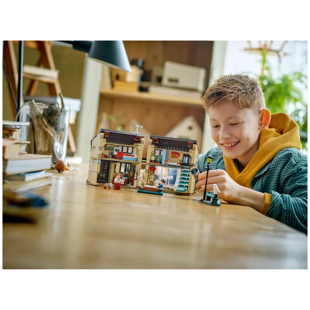 A smiling boy in a yellow hoodie plays with the LEGO Harry Potter Aunt Marge's Visit playset, showcasing detailed miniatures of 4 Privet Drive.