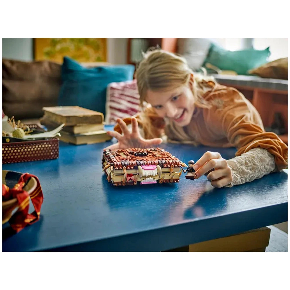 A young girl with blonde hair reaches excitedly for a LEGO® Harry Potter™ Chomping Monster Book of Monsters on a blue table, capturing the whimsical nature of the toy.