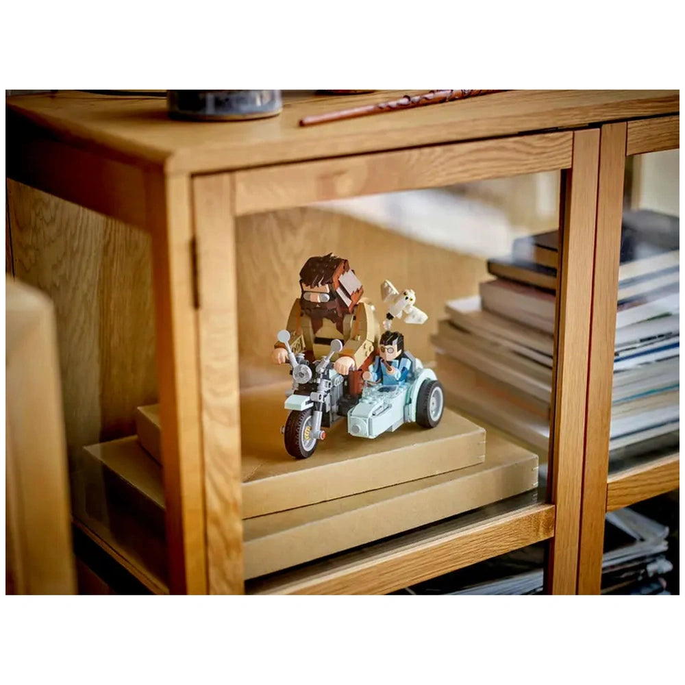 LEGO set features Hagrid and Harry on a blue motorcycle with a sidecar, Hedwig flying above, displayed in a cozy wooden cabinet.
