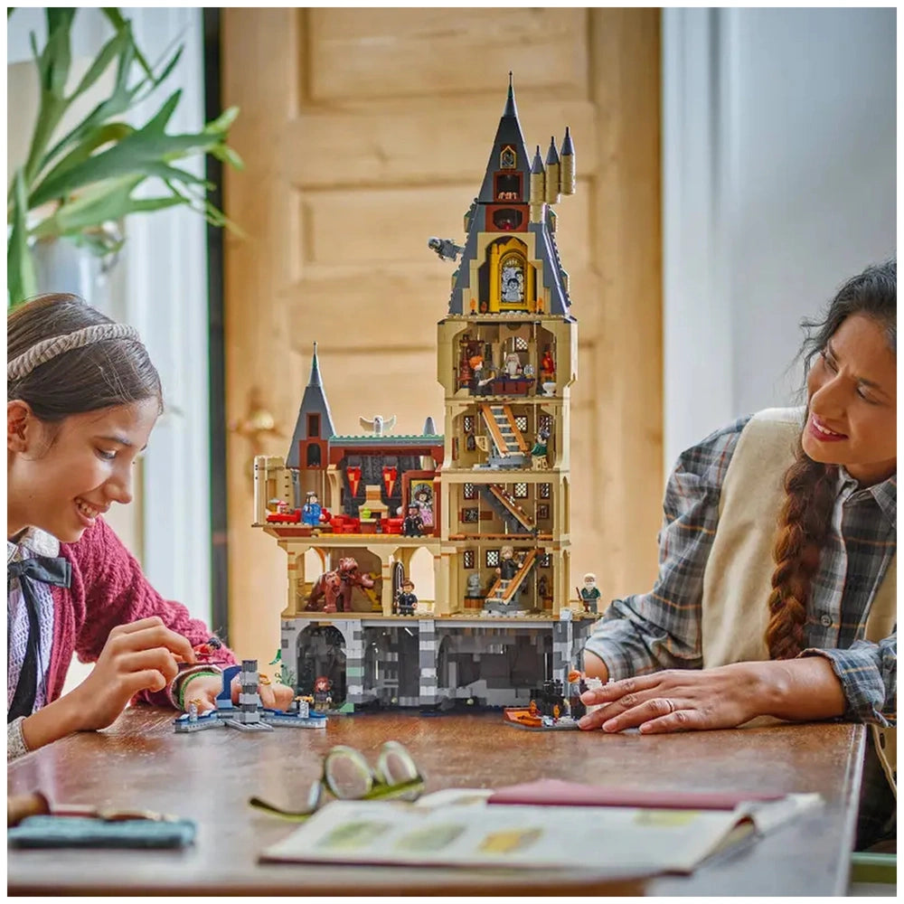 A young girl and an adult woman joyfully build the LEGO Harry Potter Hogwarts Castle set together at a table. The castle features intricate details with multiple levels, including iconic elements like Fluffy’s room and a swiveling Grand Staircase. Natural light streams in through a nearby window, illuminating their focused expressions and the colorful toy.