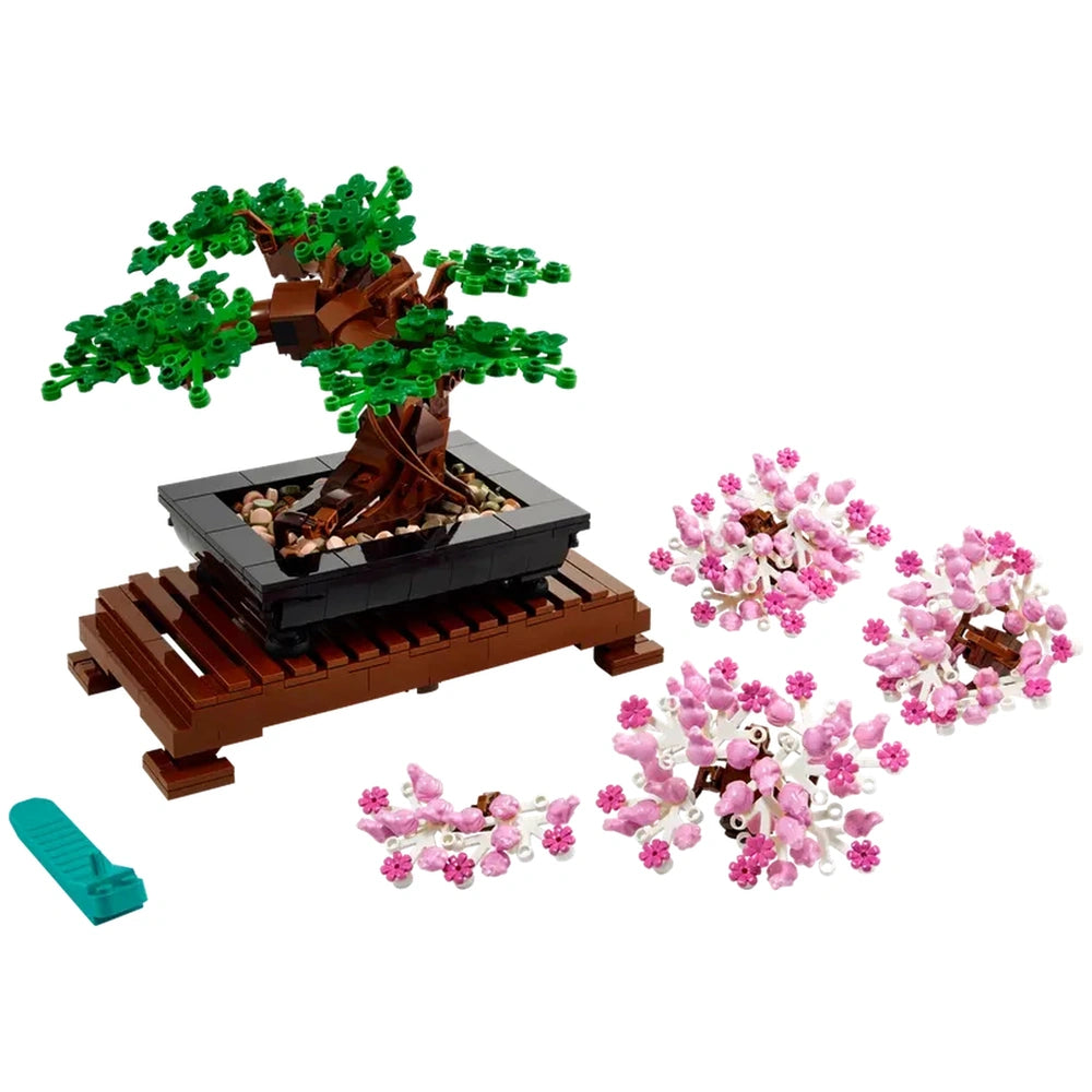 Lego Bonsai Tree construction set featuring a vibrant tree in a black pot on a wooden base, with pink cherry blossom parts scattered nearby.