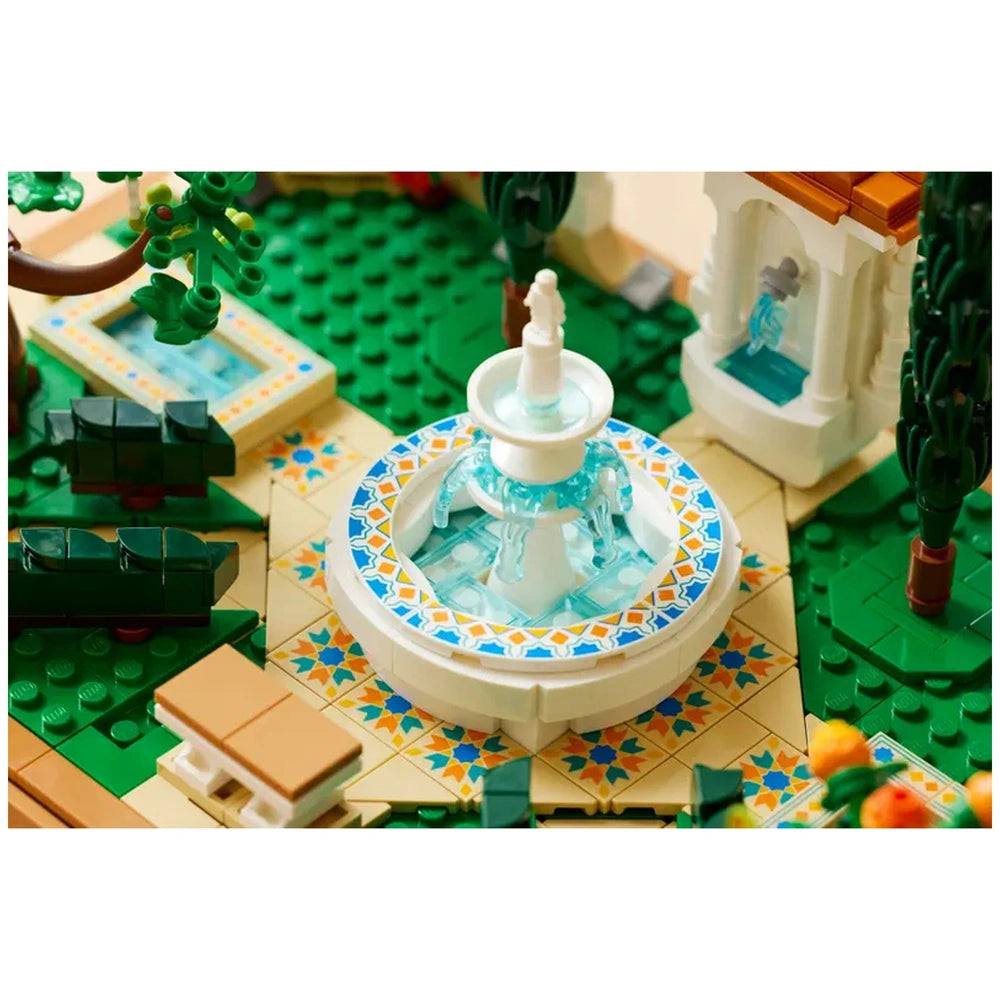 A tiered fountain with flowing water is the centerpiece of a vibrant LEGO garden, surrounded by decorative tiled pathways, green trees, and colorful flowers.