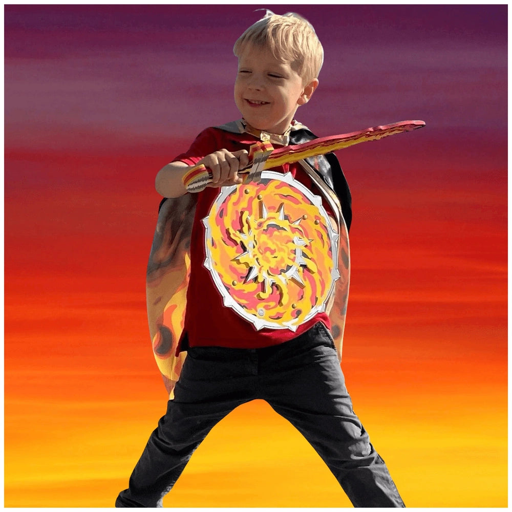 Liontouch Flame Shield in use, young boy with blonde hair in red shirt and flame-designed cape holds a sword, smiling.