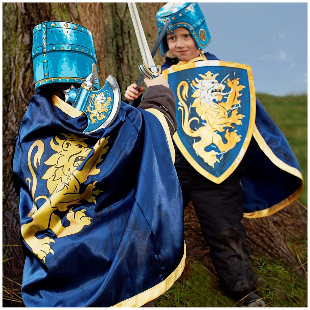 Child dressed as a knight in a blue helmet and cape with a yellow lion emblem, holding a blue sword, standing by a tree.