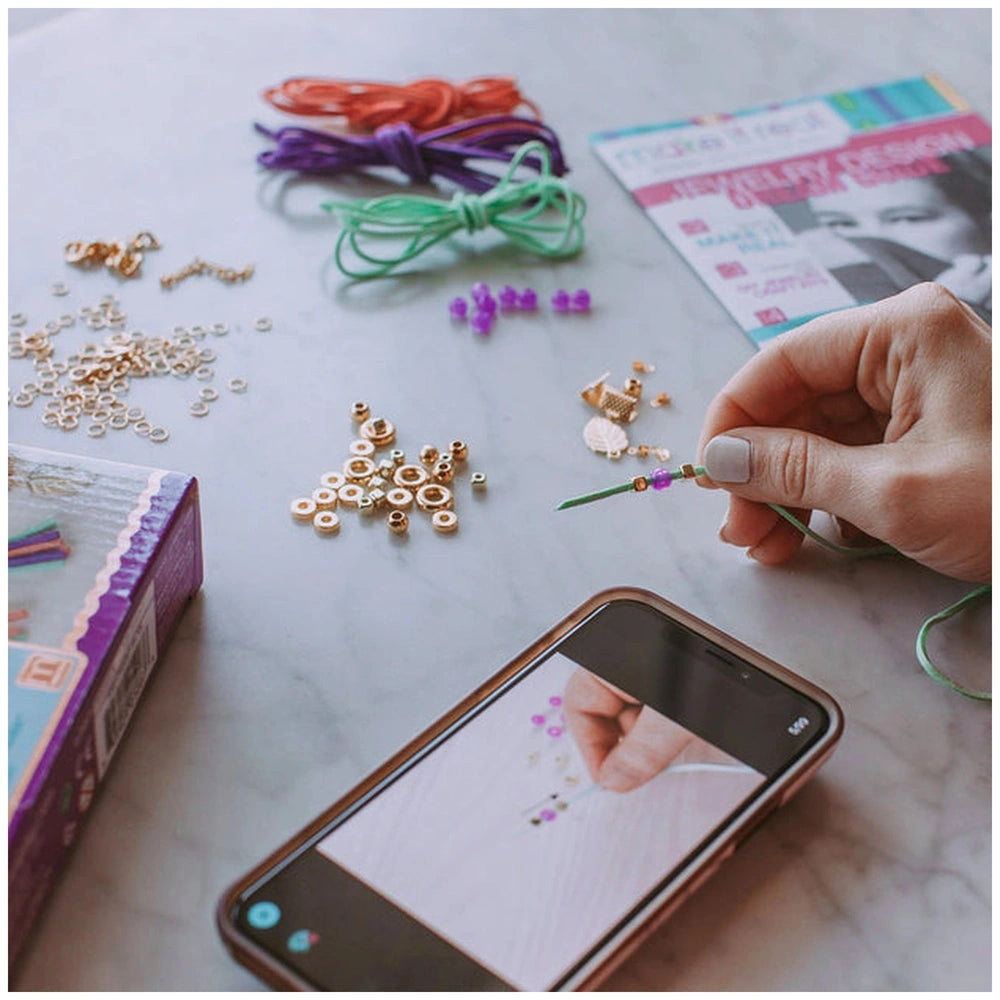 Gold link suede bracelets with assorted beads and wires on a marble countertop, hand holding green wire and purple bead.
