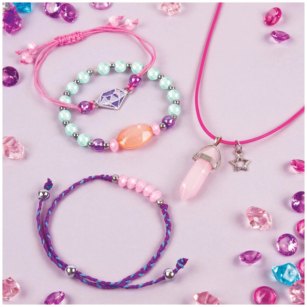 Positive Gems Jewelry features colorful bracelets with translucent beads and a star pendant necklace on a stone-strewn surfac