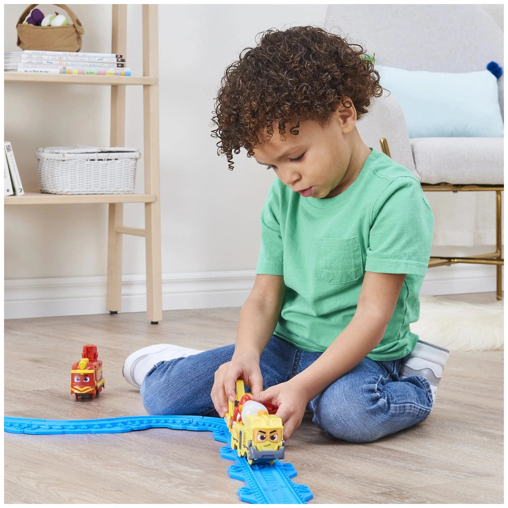 Mighty Express motorized train in front of a child sitting on a light wooden floor with colorful books and a blue-cushioned c