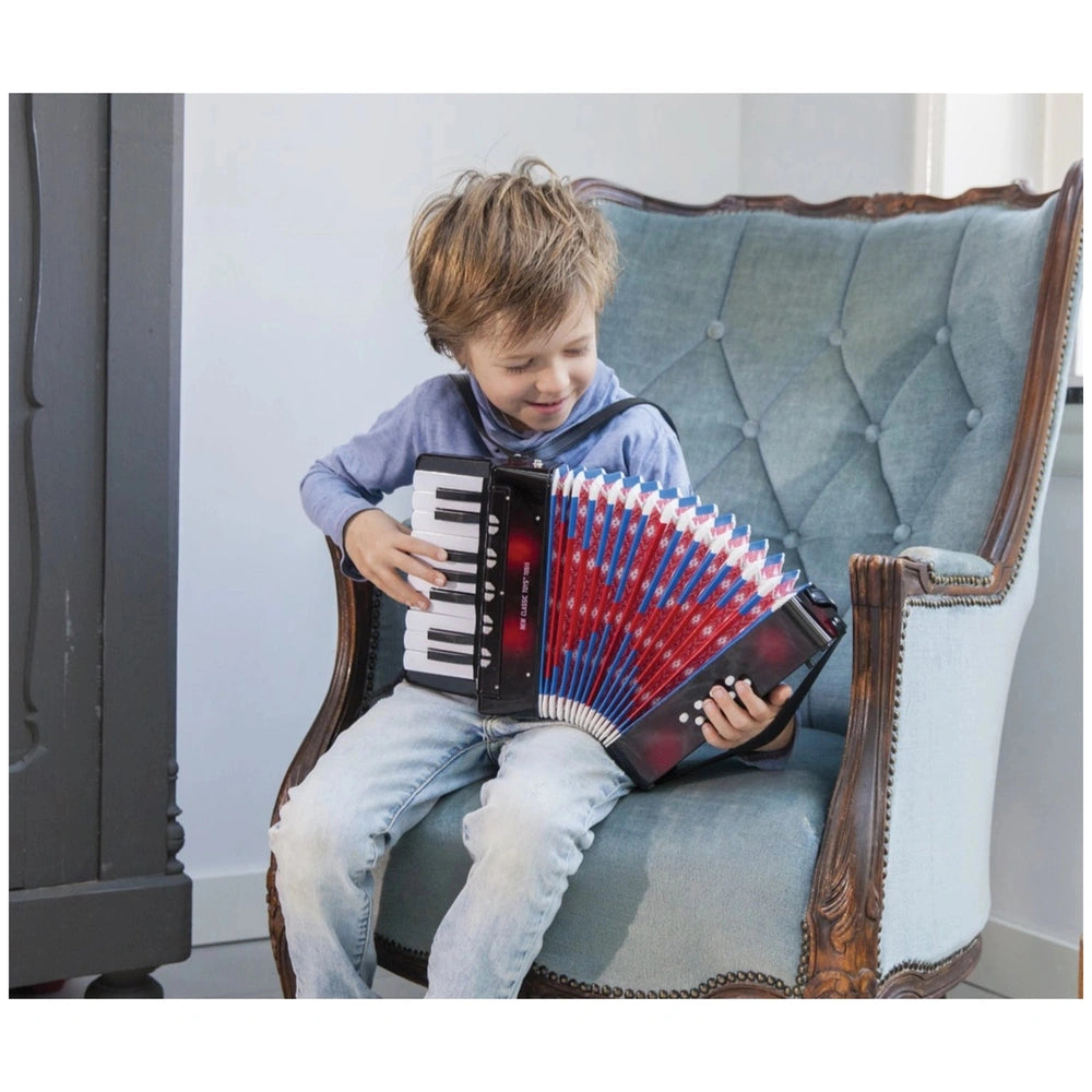 Black accordion with music book held by a young boy in a blue shirt and jeans, sitting on a blue upholstered chair.