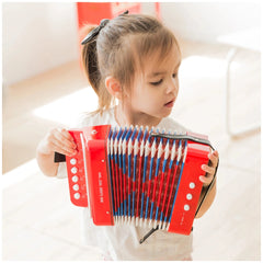 Blonde girl in a white top holds a red accordion with blue and red keys, featuring white buttons and a black strap.