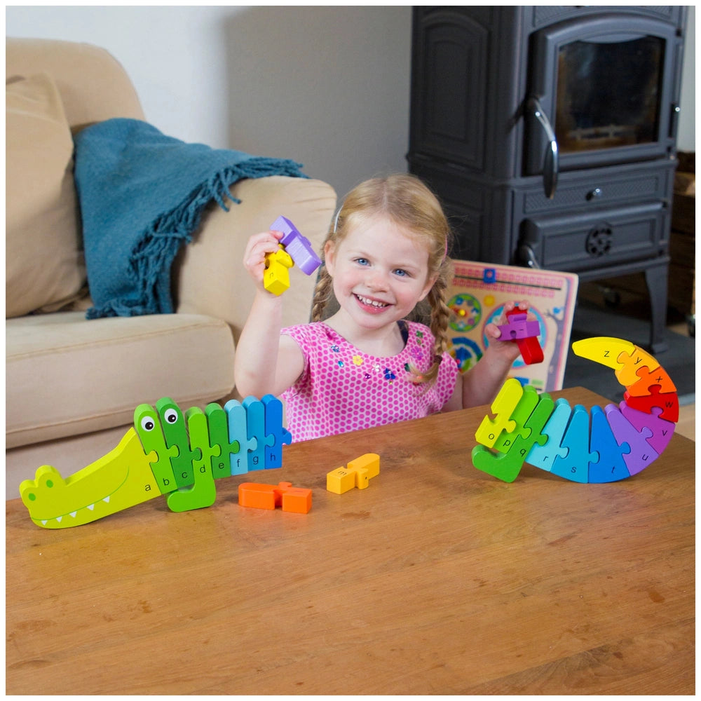 Young girl in a pink dress smiles while playing with colorful plastic toys on a wooden table in a cozy living room.