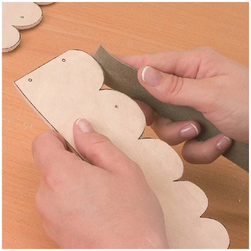 Hands sanding a wooden cutout with a scalloped edge, part of the Prebaro Fretwork Kit in a woodworking project.