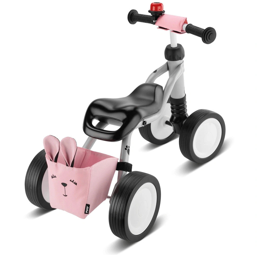 Puky Wutsch pink and gray metal quadricycle features a white frame, black seat, and a pink fabric basket with a black handle.