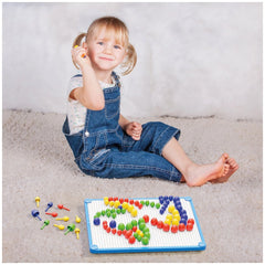 Young girl in denim jumpsuit smiles while playing with colorful Quercetti FantaColor Tab objects on a fluffy white rug.